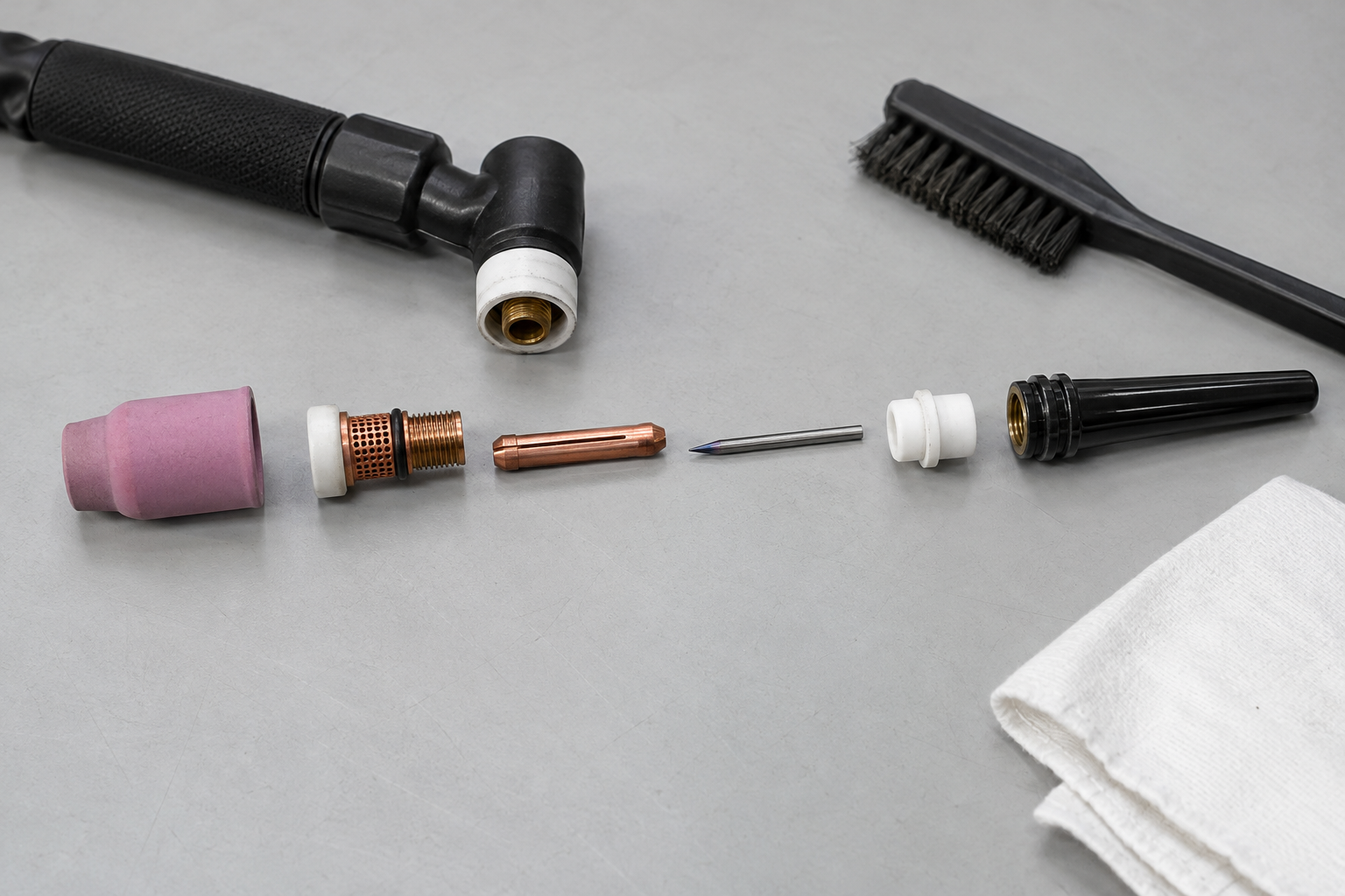 Disassembled TIG torch head with cup, gas lens, collet, tungsten, insulator, and back cap arranged for inspection